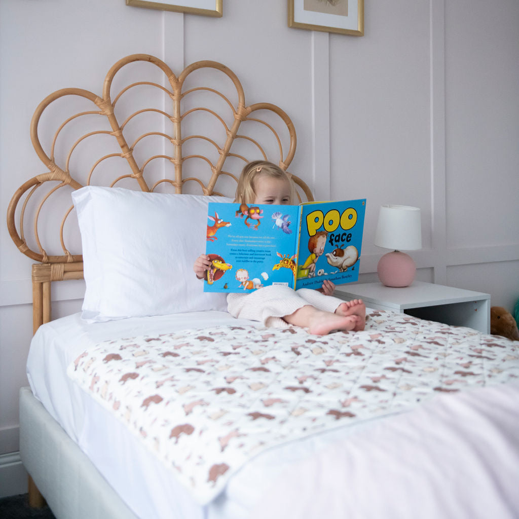 Child reading a book on a bed with decorative headboard and framed pictures on the wall.
