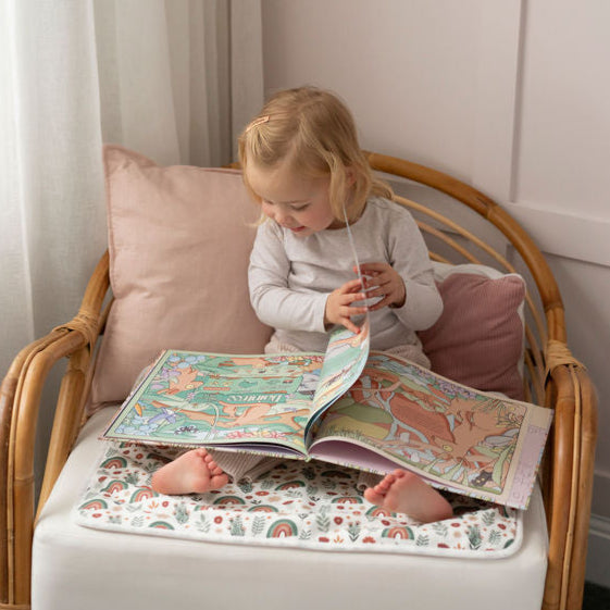 
                      
                        Child sitting on a small chair with a Spewy mat underneath for protection, reading a book in a cozy room.
                      
                    