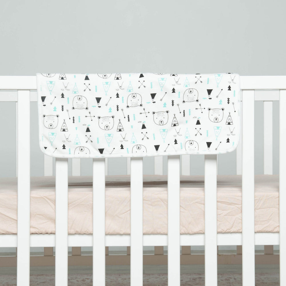 
                      
                        White crib with a white mattress featuring black and blue geometric patterns on a gray background
                      
                    