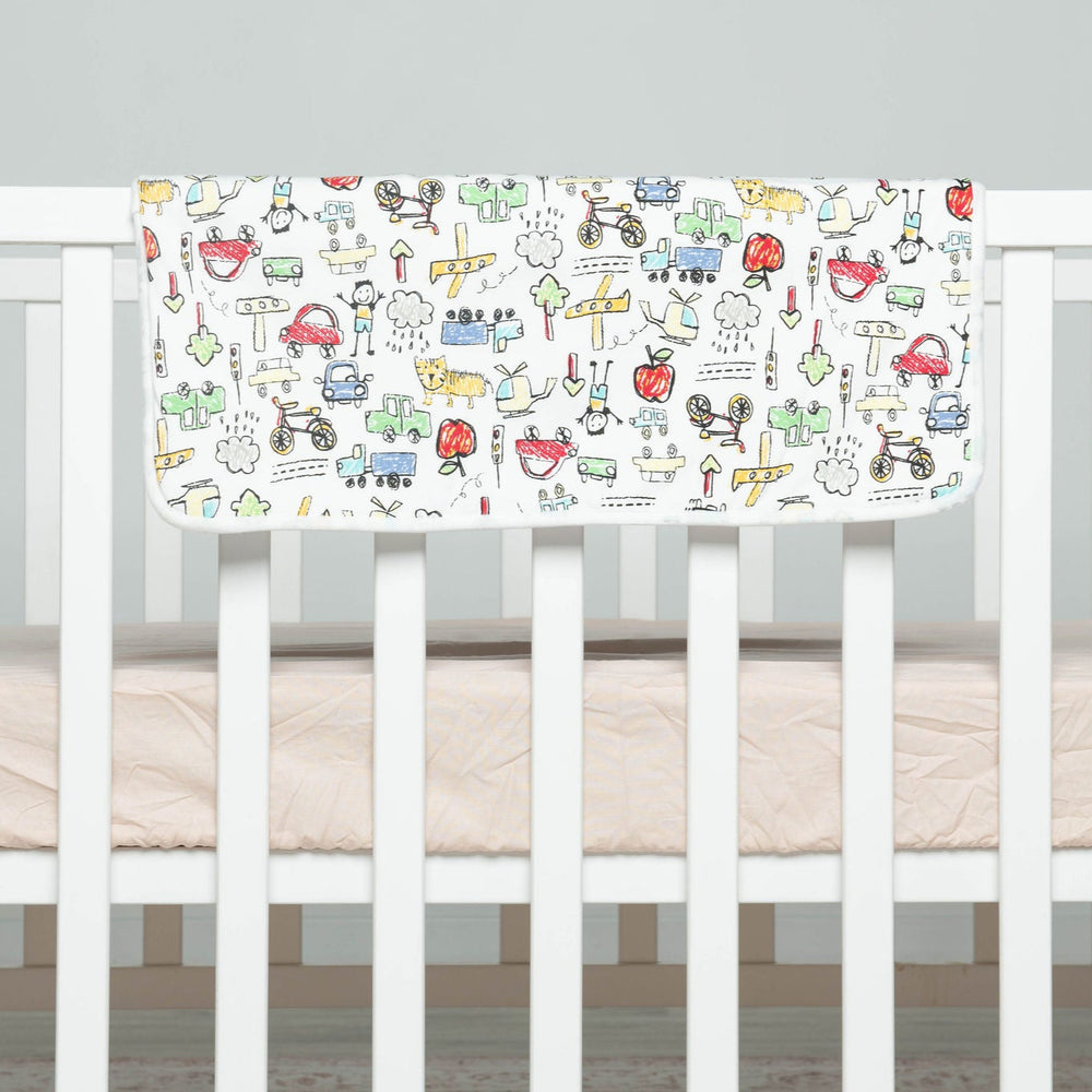 
                      
                        Crib with a colorful baby blanket featuring illustrations of animals and vehicles on a white background.
                      
                    