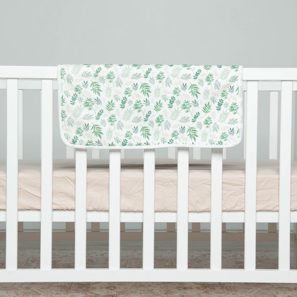 
                      
                        White crib with a green leaf-patterned blanket on a gray background
                      
                    