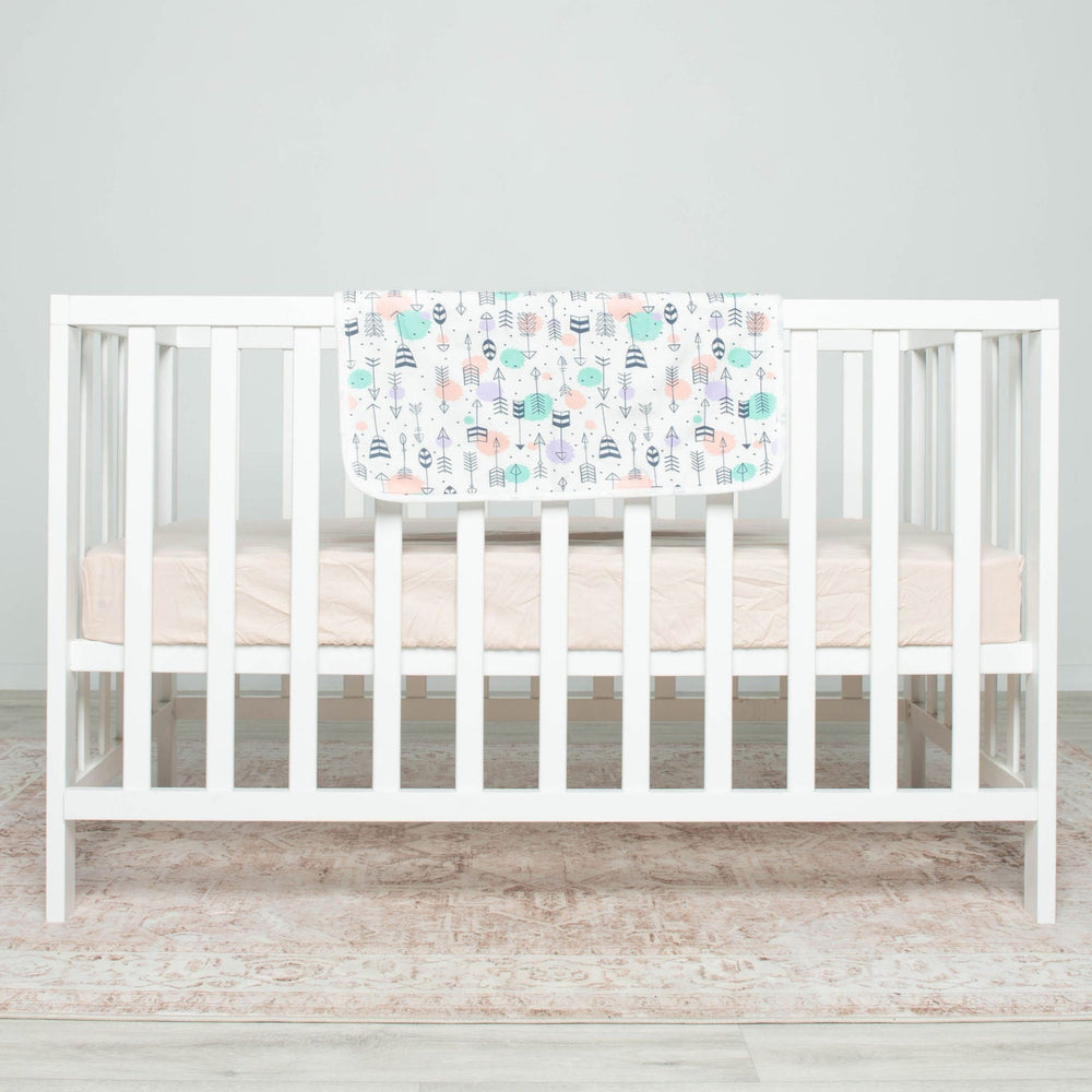 
                      
                        White crib with a Polka Arrow Spewy on a light wooden floor and gray wall background
                      
                    